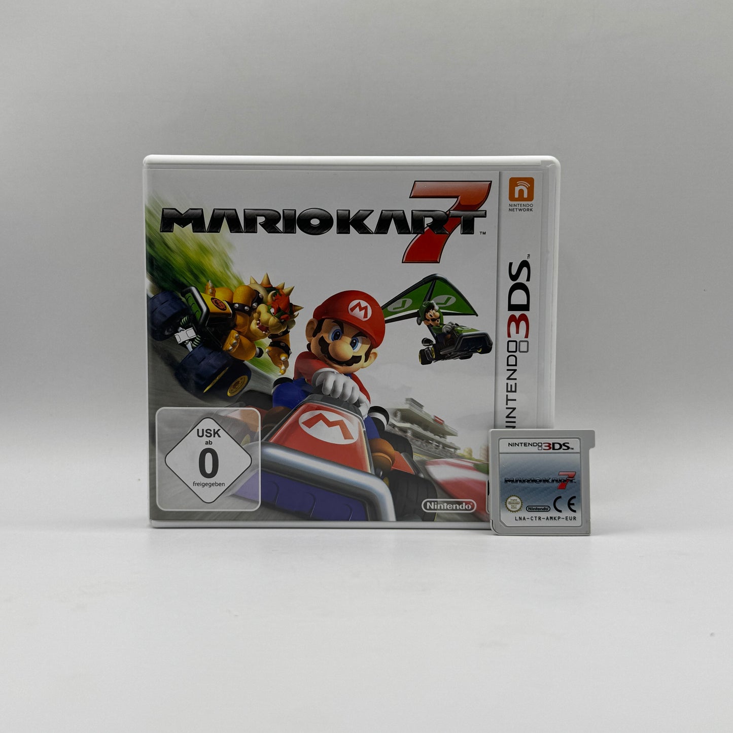 Verpackung des Nintendo 3DS-Spiels Mario Kart 7, ein Rennspiel, in dem Spieler als Mario-Charaktere auf verschiedenen Strecken gegeneinander antreten und Items einsetzen, um Vorteile zu gewinnen.