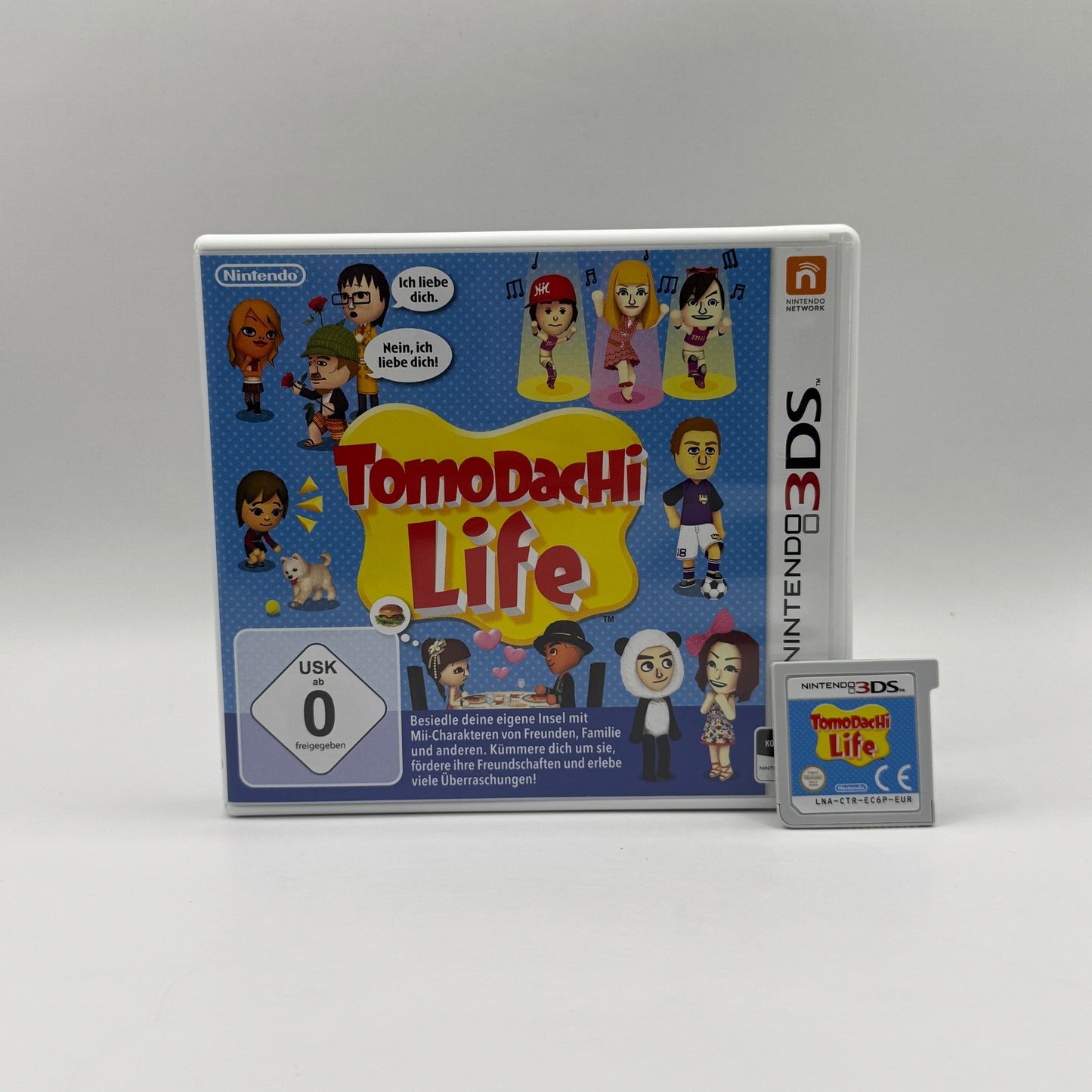 Verpackung des Nintendo 3DS-Spiels Tomodachi Life, eine Lebenssimulation, in der Spieler Mii-Charaktere erstellen, auf einer Insel leben lassen und deren Beziehungen, Alltagsleben und verrückte Ereignisse beobachten.