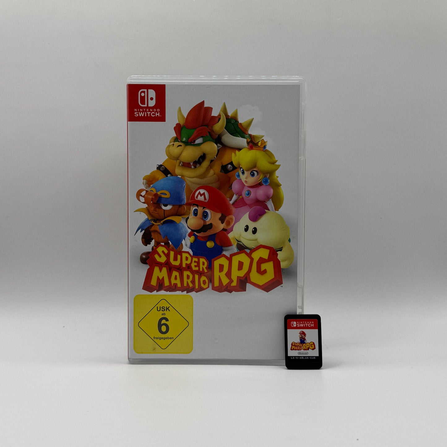 Verpackung des Switch-Spiels Super Mario RPG, ein Rollenspiel, in dem Spieler Mario und seine Freunde steuern, rundenbasierte Kämpfe bestreiten und Abenteuer in einer fantasievollen Welt erleben.