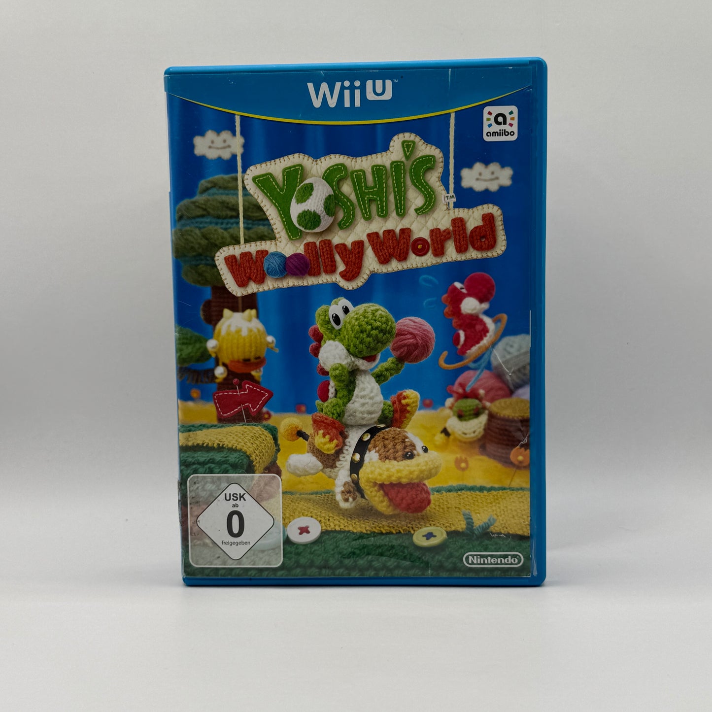 Verpackung des Wii U-Spiels Yoshi’s Woolly World, ein 2D-Platformer, in dem Spieler Yoshi durch handgemachte, wollige Level steuern, Gegner besiegen und Rätsel lösen.