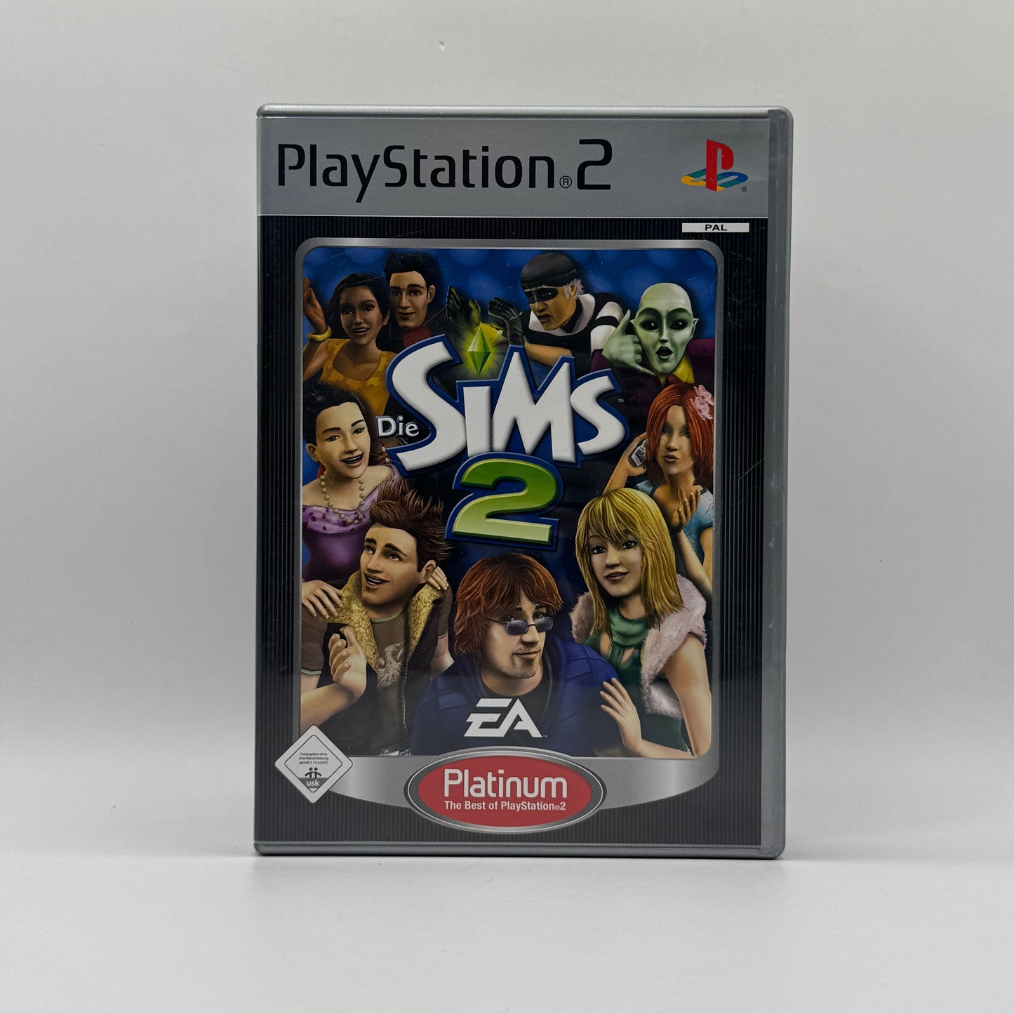 Verpackung des PS2-Spiels Die Sims 2 in der Platinum-Edition, eine Lebenssimulation, in der Spieler Sims erstellen, Häuser bauen und deren Alltag sowie Lebenswege steuern.