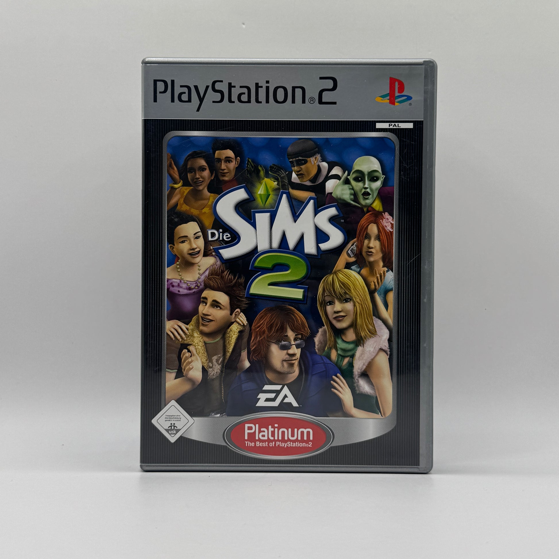 Verpackung des PS2-Spiels Die Sims 2 in der Platinum-Edition, eine Lebenssimulation, in der Spieler Sims erstellen, Häuser bauen und deren Alltag sowie Lebenswege steuern.